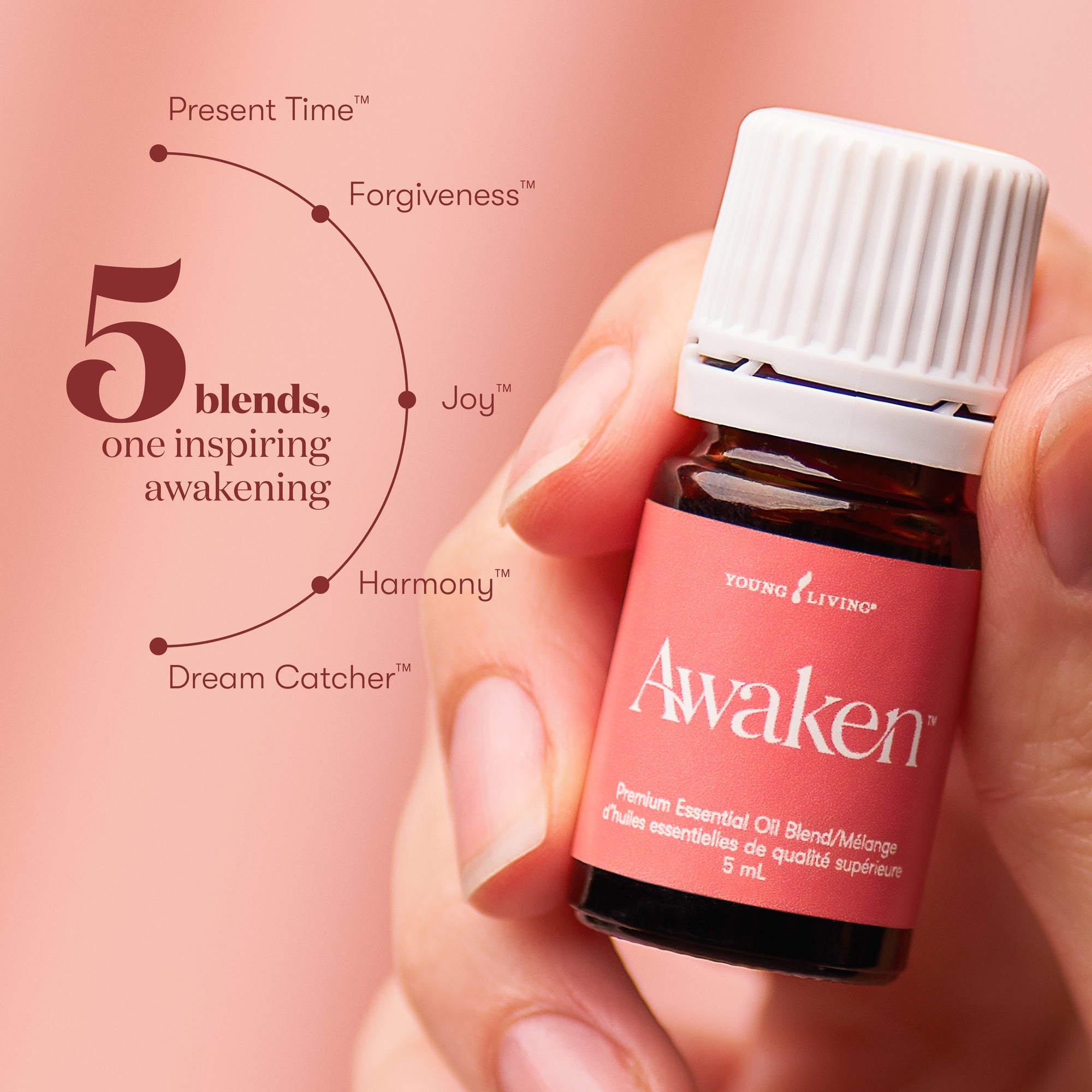 Hand holding a Young Living Awaken essential oil bottle with a pink background and text about different blends.