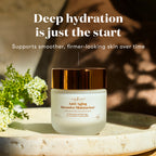 A jar of Anti-Aging Intensive Moisturizer sits on a stone surface with white flowers and a warm, sunlit background. Text above reads, 'Deep hydration is just the start' and 'Supports smoother, firmer-looking skin over time.