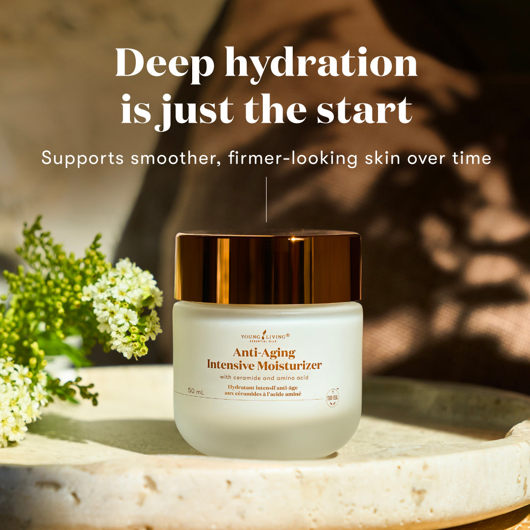 A jar of Anti-Aging Intensive Moisturizer sits on a stone surface with white flowers and a warm, sunlit background. Text above reads, 'Deep hydration is just the start' and 'Supports smoother, firmer-looking skin over time.
