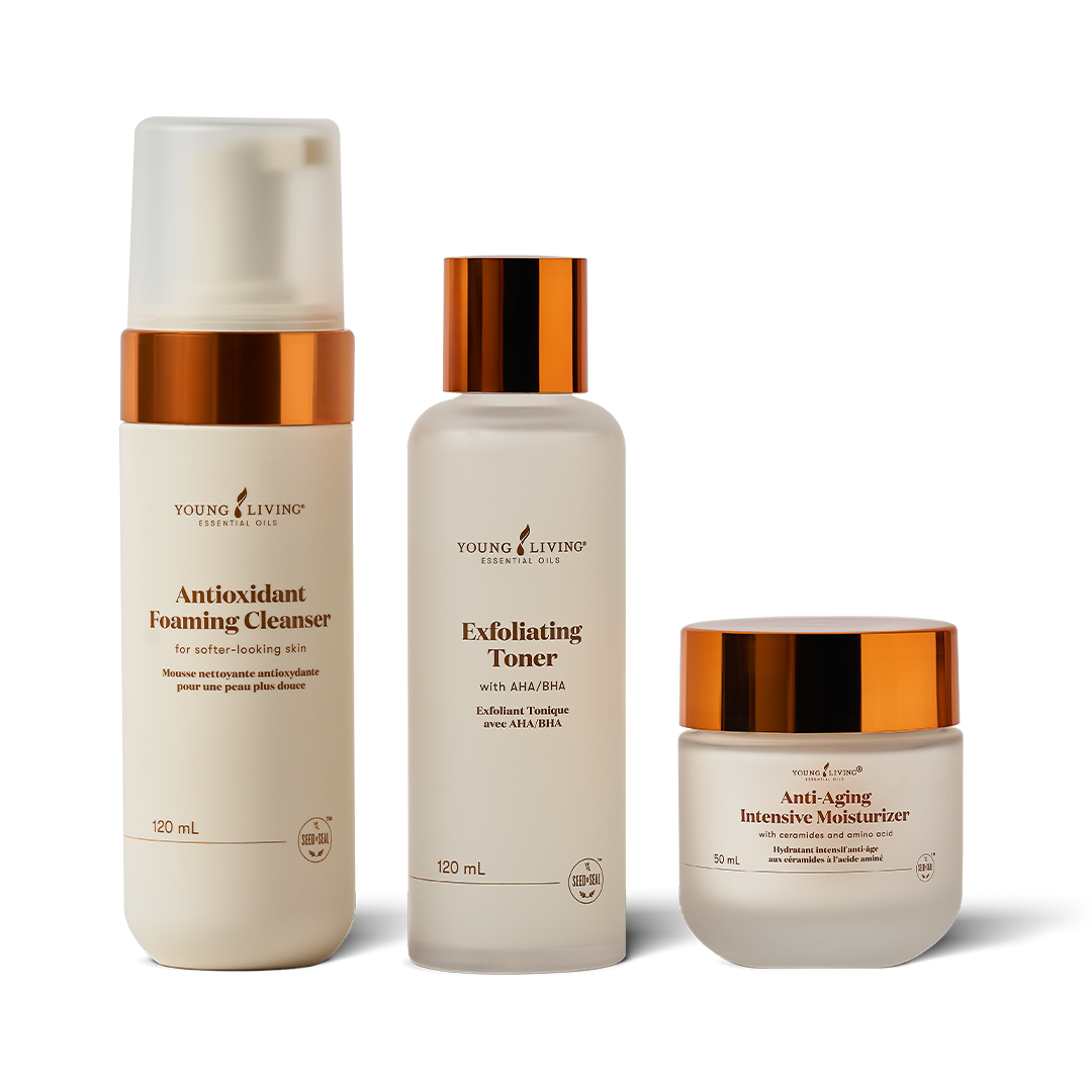 Three skincare products from Young Living on a white background: a frosted bottle of Antioxidant Foaming Cleanser, a frosted bottle of Exfoliating Toner with a metallic copper cap, and a frosted jar of Anti-Aging Intensive Moisturizer with a metallic copper lid.