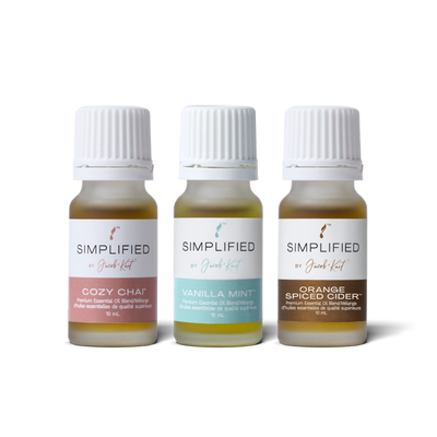 Three small glass essential oil bottles of Simplified by Jacob + Kait arranged side by side on a white background. The labels read Cozy Chai, Vanilla Mint, and Orange Spiced Cider.